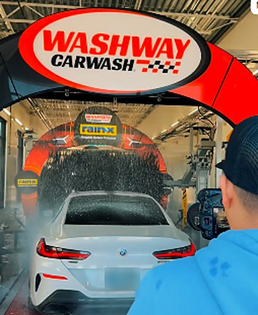 A white car entering the Washway Car Wash tunnel under the red Washway arch